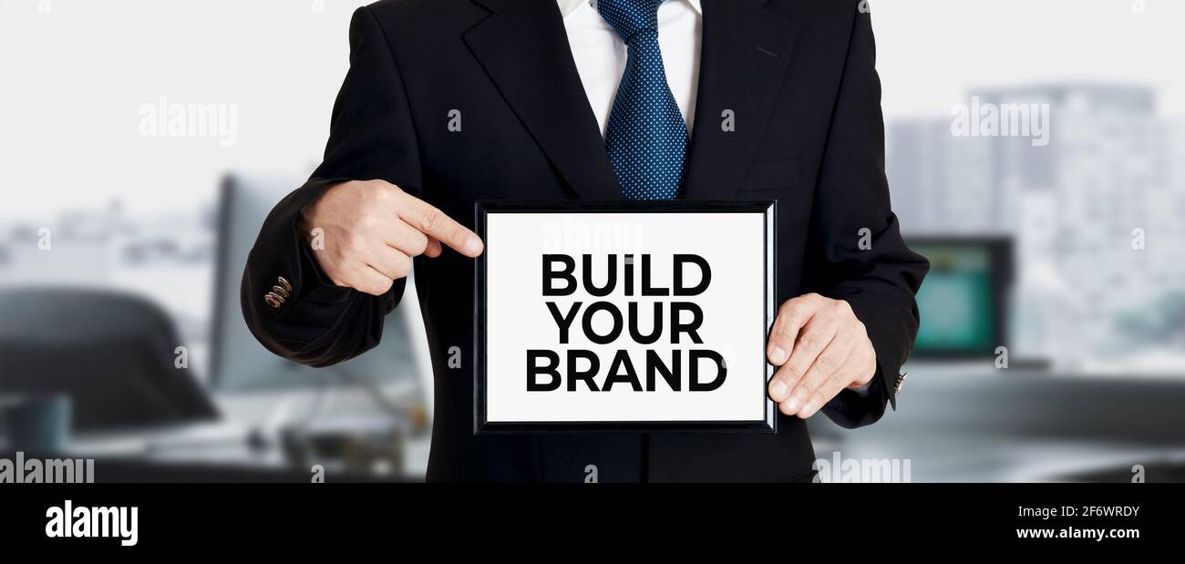 L'uomo d'affari tiene un cartello e punta il suo dito al messaggio costruire il vostro marchio. Brand building nel business marketing. Foto Stock