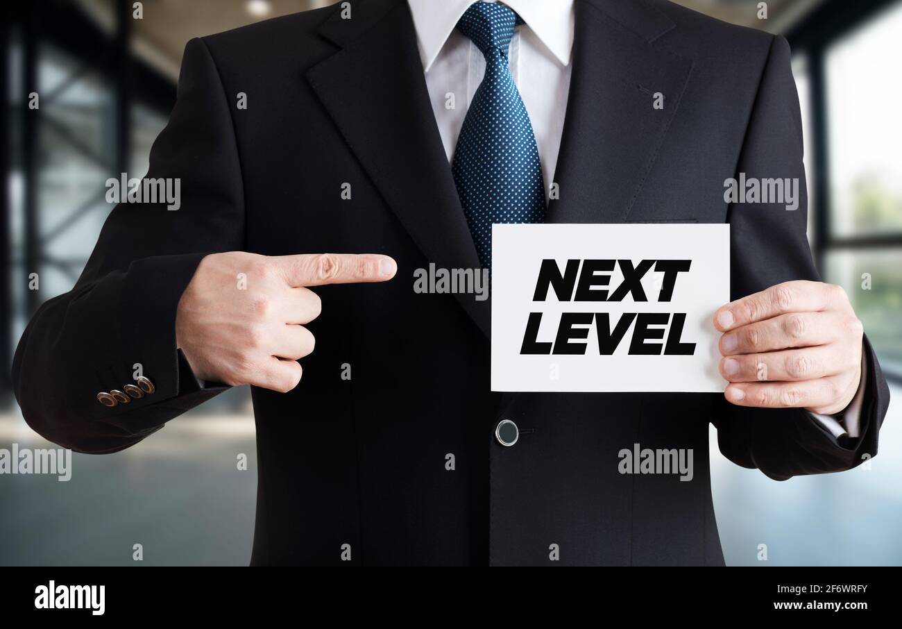 Uomo d'affari mostra una scheda con il messaggio di livello successivo. Progresso, crescita, sviluppo o miglioramento del concetto di carriera aziendale. Foto Stock