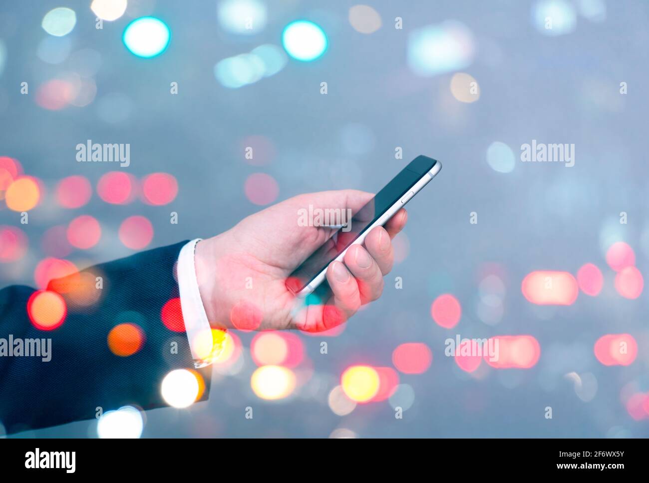 Uomo d'affari che tiene in mano smartphone e sfondo della città con traffico e auto, business concept immagine Foto Stock