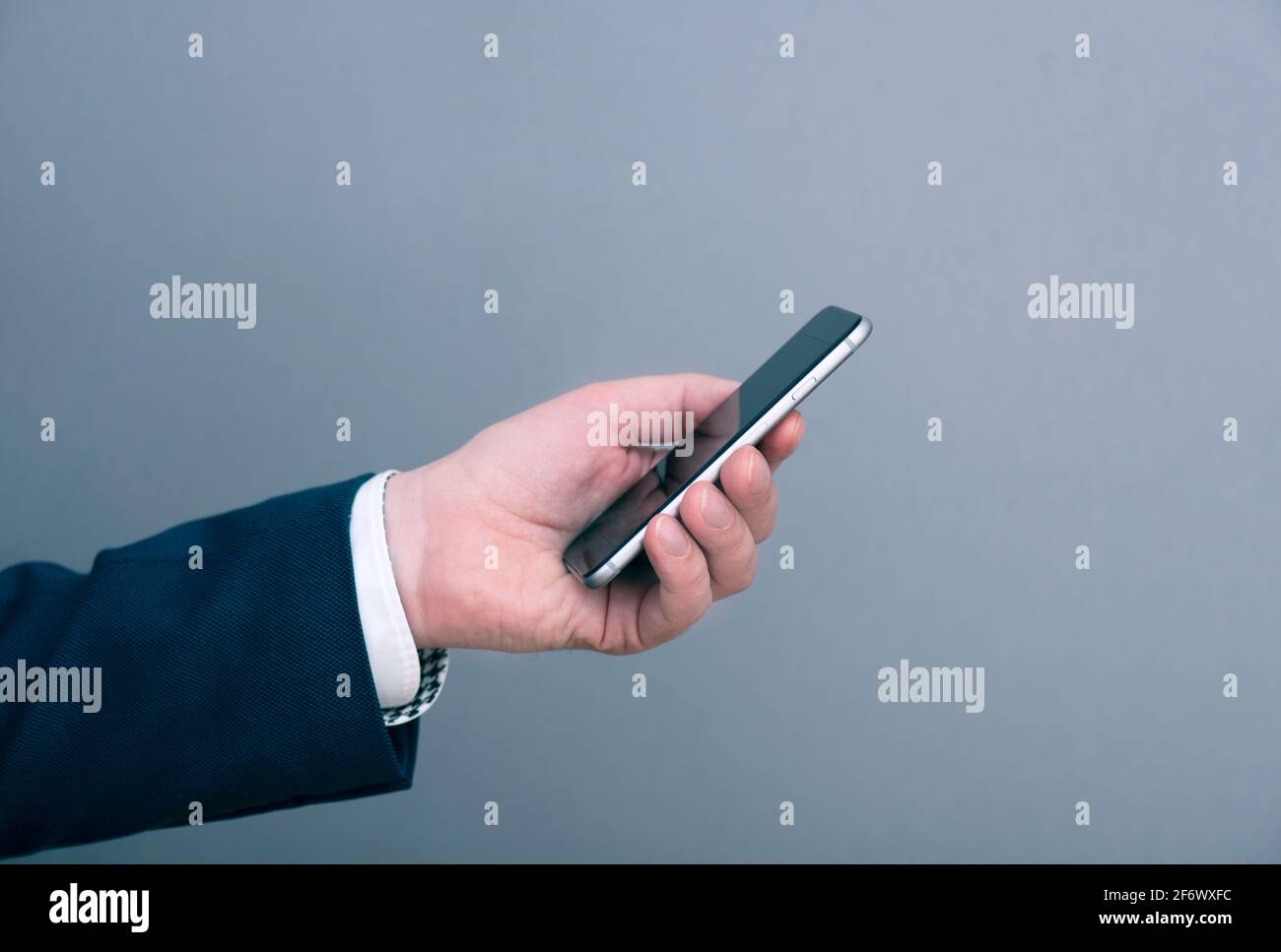 Un uomo d'affari vestito in abito che tiene smartphone di fronte a sfondo grigio. Immagine del concetto di business. Foto Stock