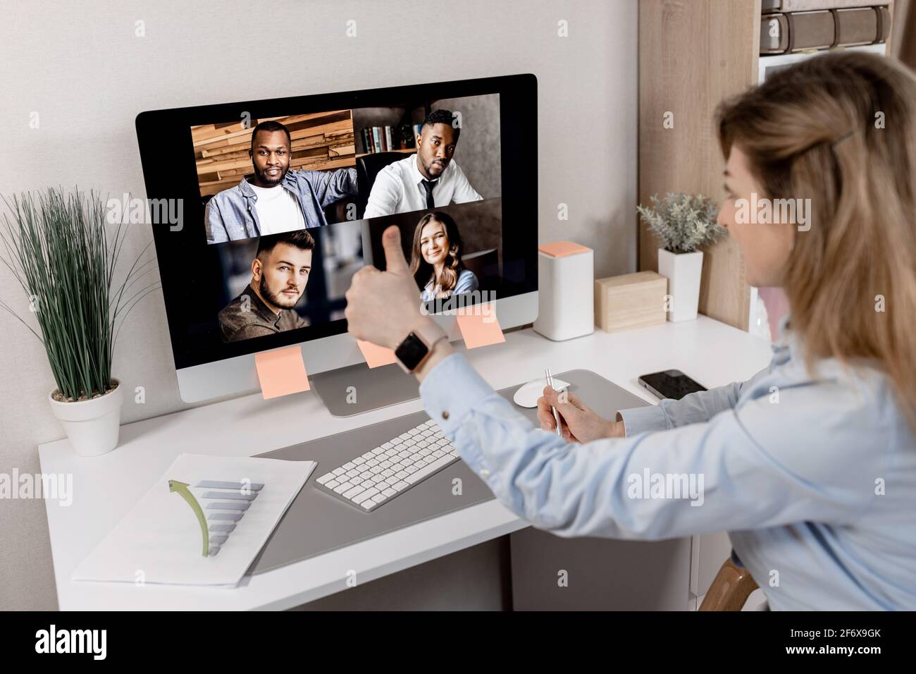 Vista posteriore di una bella dipendente femminile di stile che mostra i pollici ai colleghi durante la riunione online. Elegante donna d'affari in abbigliamento formale da lavoro Foto Stock