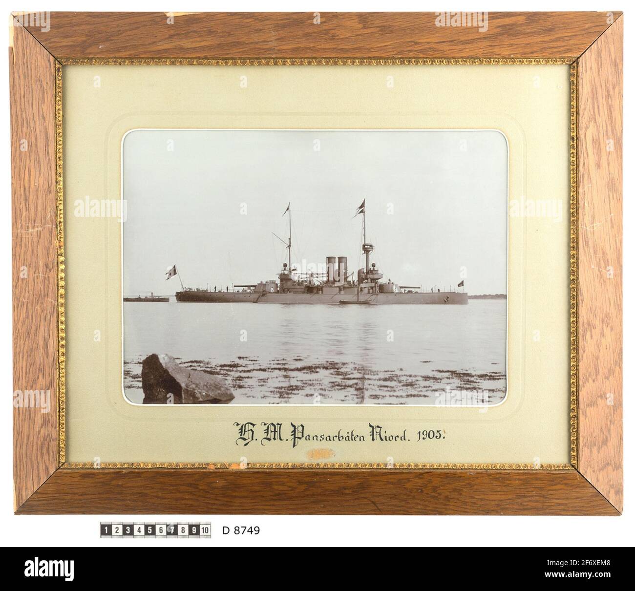 Il ritratto della nave che mostra la barca armata Niord ad Ankars.The nave è visibile dal lato del porto dove una nave è ormeggiata.parecchie scale di corda conduce fino al Tyre.at la poppa è una piccola barca a vapore che sembra sostenere la barca armor.on il deposito, Due lavoro but.The sfondo mostra la costa.The primo piano è dominato da un grande massi e si aspetta il bordo della costa a causa di alghe in acqua .. Il ritratto di spedizione che mostra la barca armata Niord ad Ankars.The nave è visibile dal lato del porto dove una nave è ormeggiata.parecchie scale di corda conduce fino al pneumatico.at la poppa è un piccolo vapore bo Foto Stock