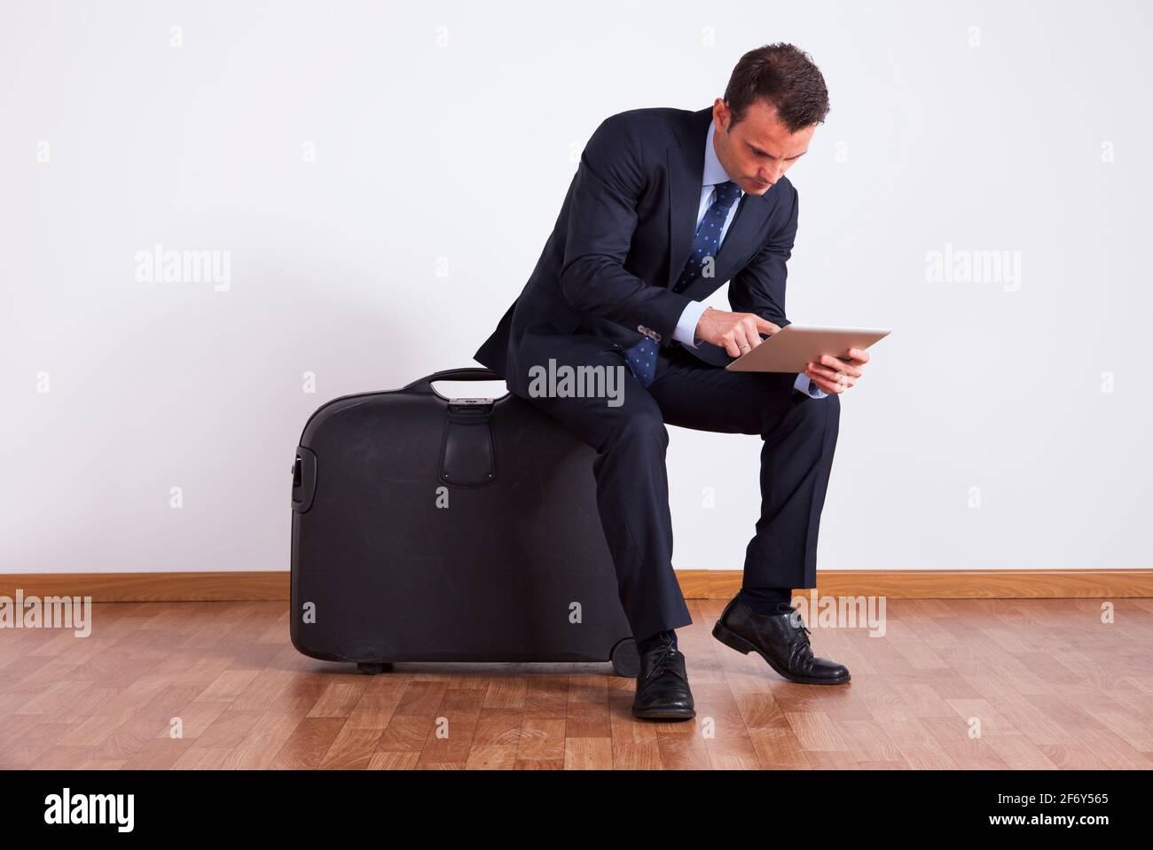 Un uomo d'affari si siede su un bagaglio da viaggio utilizzando un tablet digitale Foto Stock