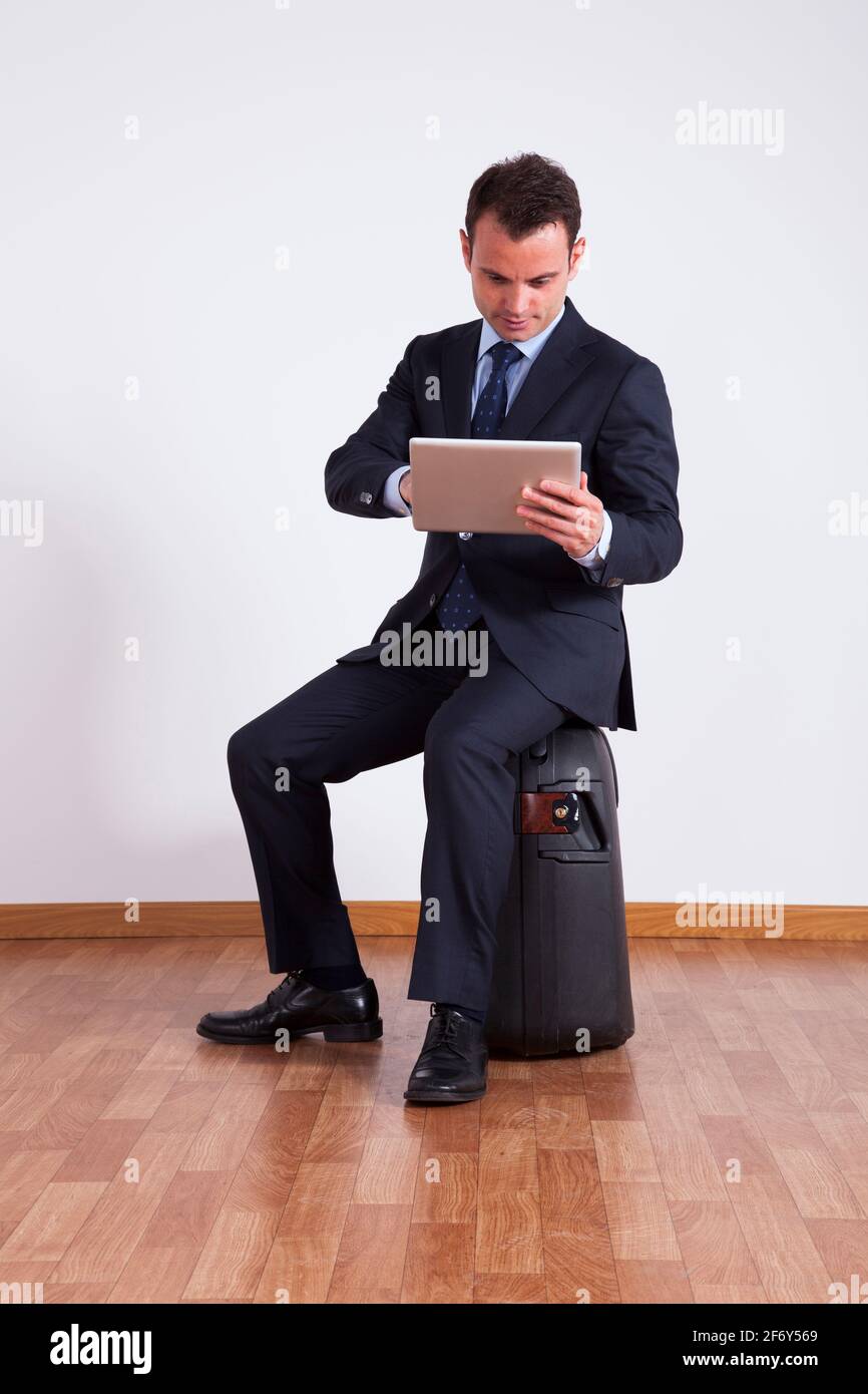 Un uomo d'affari si siede su un bagaglio da viaggio utilizzando un tablet digitale Foto Stock