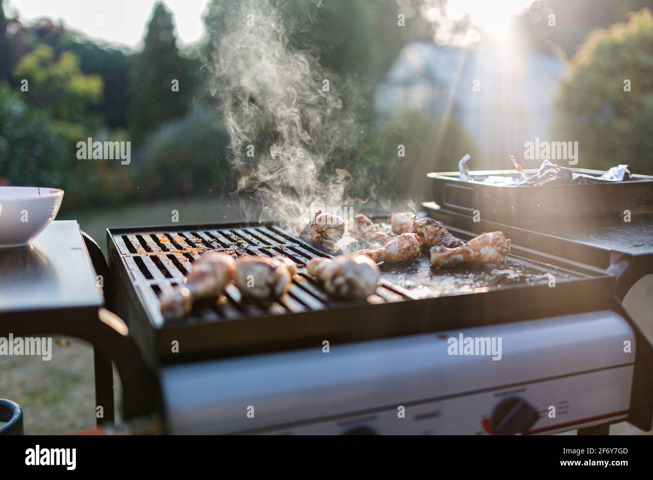 Primo piano di una griglia barbecue con carne che cucinano su di loro, luce solare sullo sfondo sta catturando il fumo Foto Stock