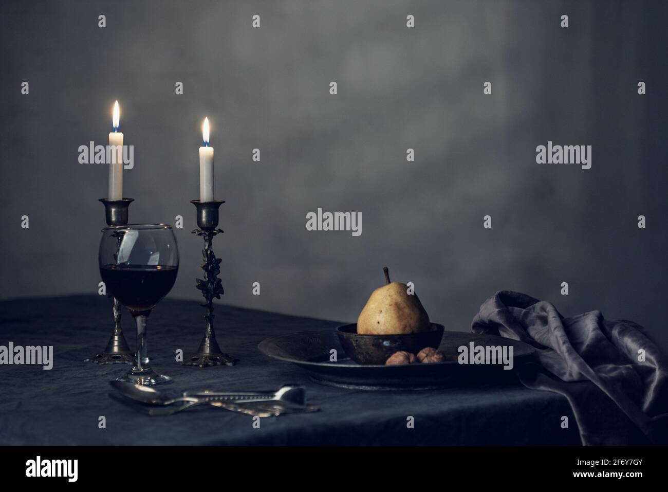 Un bicchiere di vino con candele bianche e una pera su un panno da tavola di colore scuro, fotografia di natura morta, fotografia isolata, interna Foto Stock