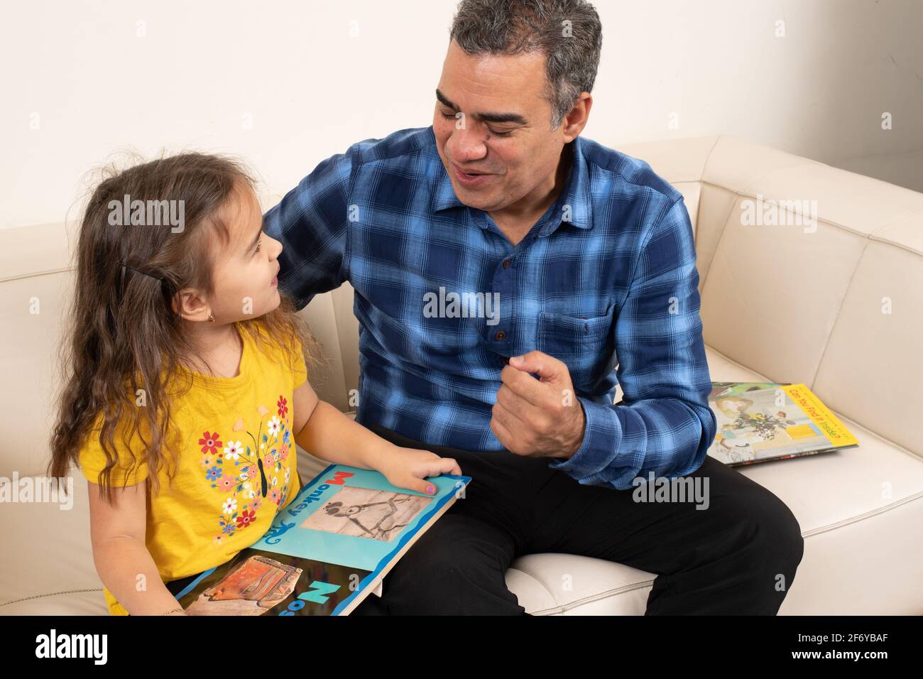 Bambina di quattro anni che guarda un libro di immagini con nonno, parlando e interagendo con lui Foto Stock