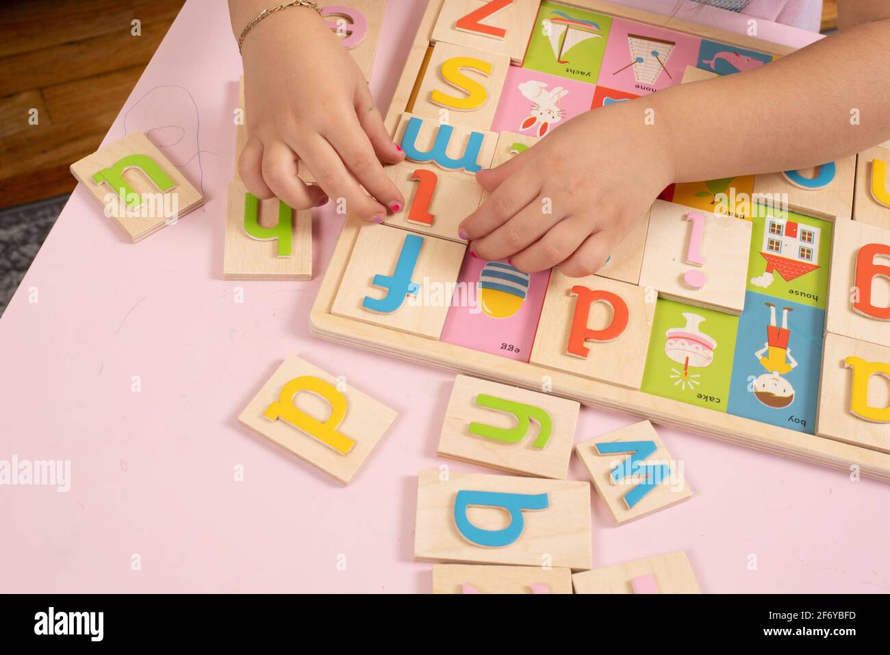 Ragazza di quattro anni che gioca con closeup puzzle alfabeto in legno delle sue mani al lavoro tra le lettere colorate Foto Stock