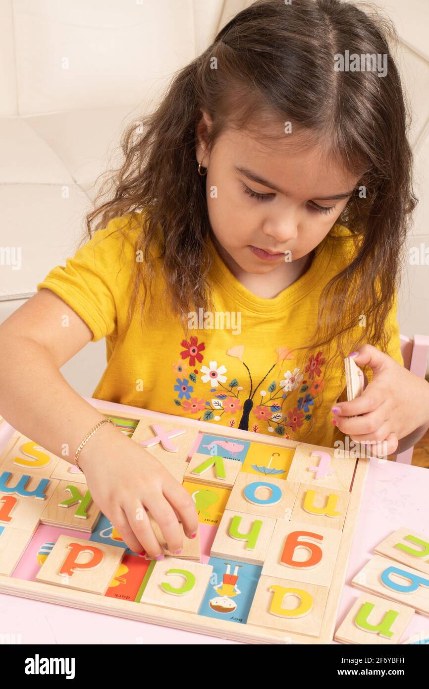 Ragazza di quattro anni che gioca con puzzle alfabeto in legno, mettendo lettere colorate nei loro punti Foto Stock