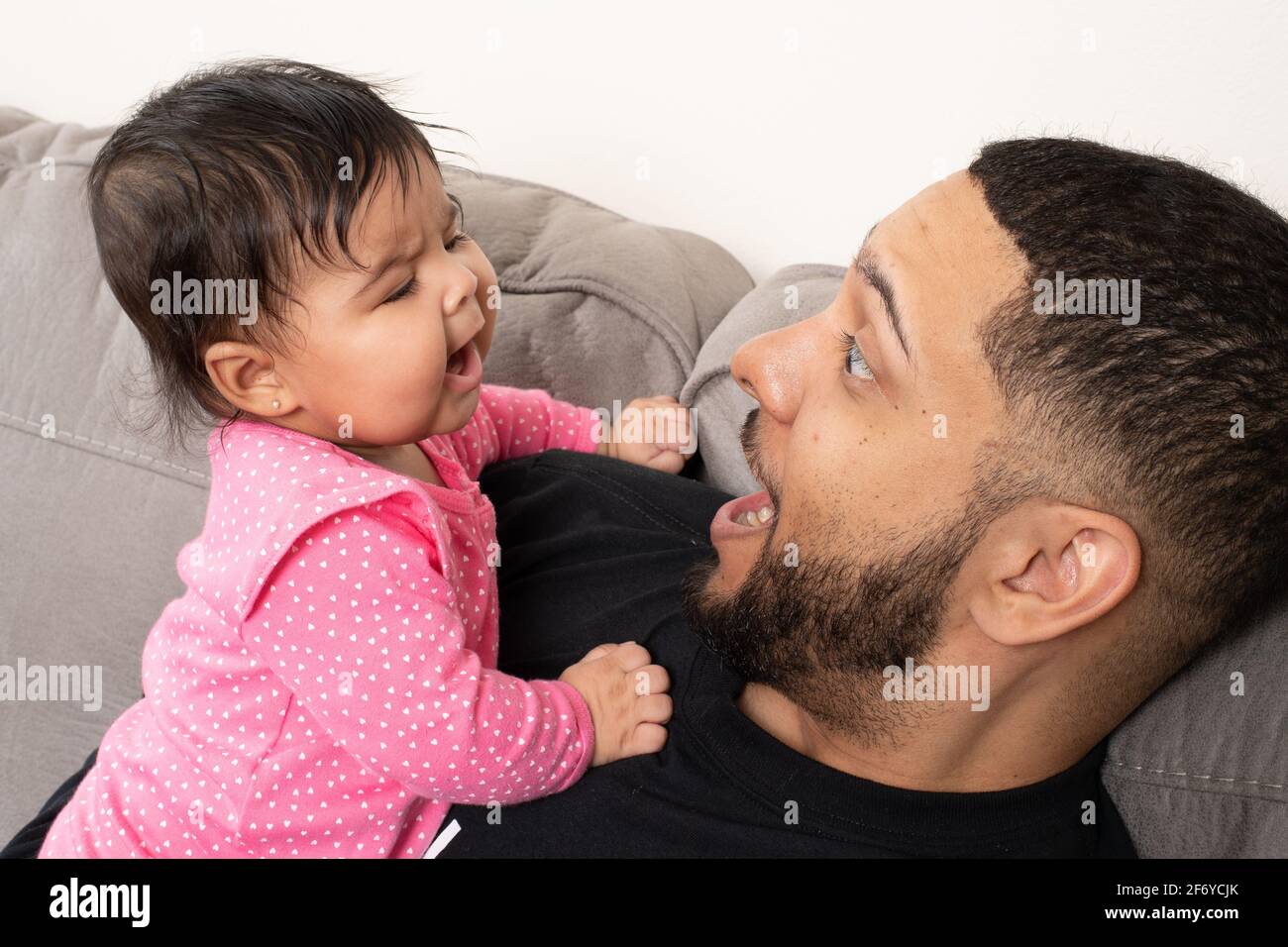 Padre che tiene e interagisce con la bambina di 4 mesi, espressioni di corrispondenza Foto Stock