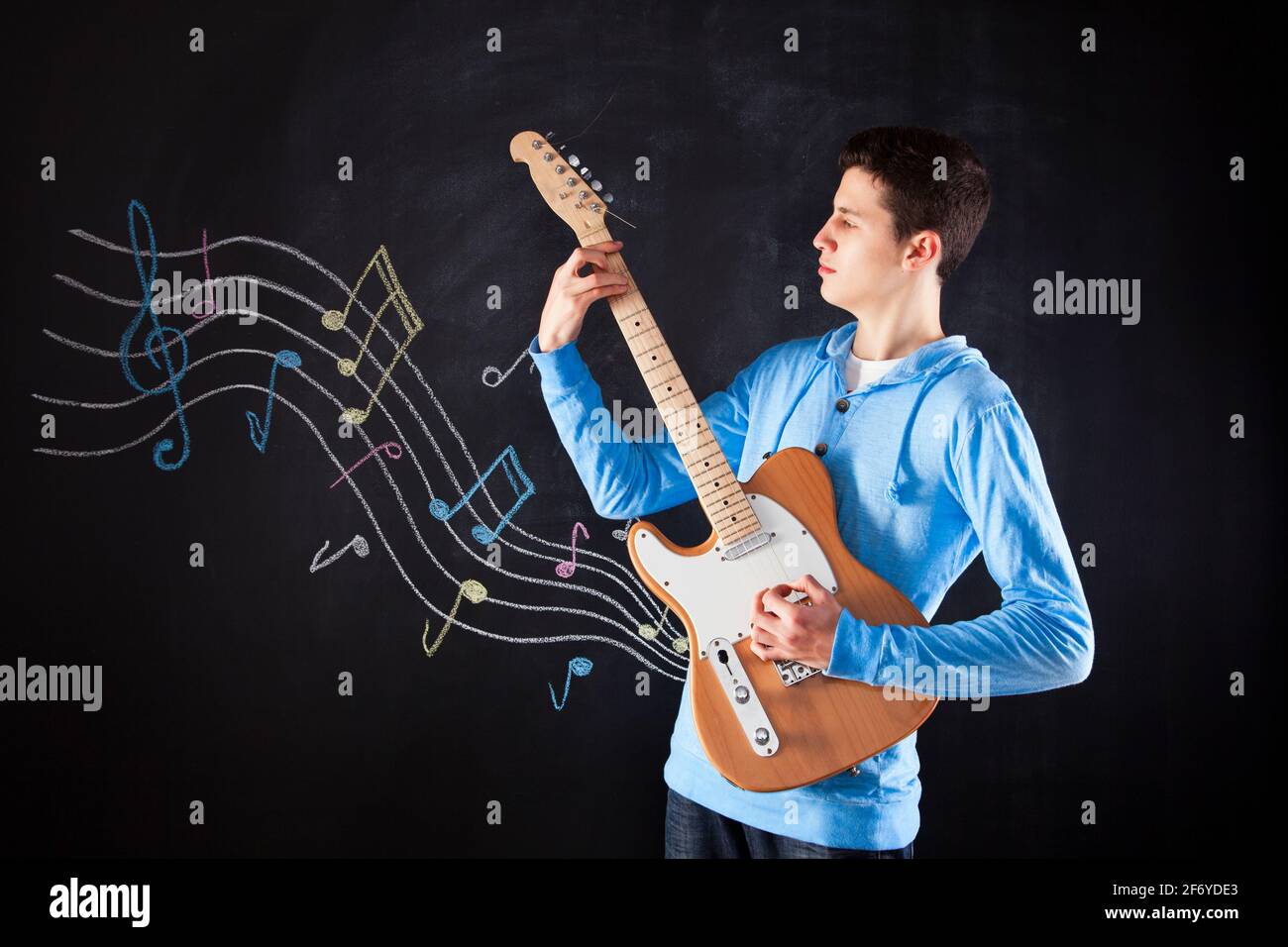 Adolescente che tiene una chitarra elettrica accanto a una lavagna Foto Stock