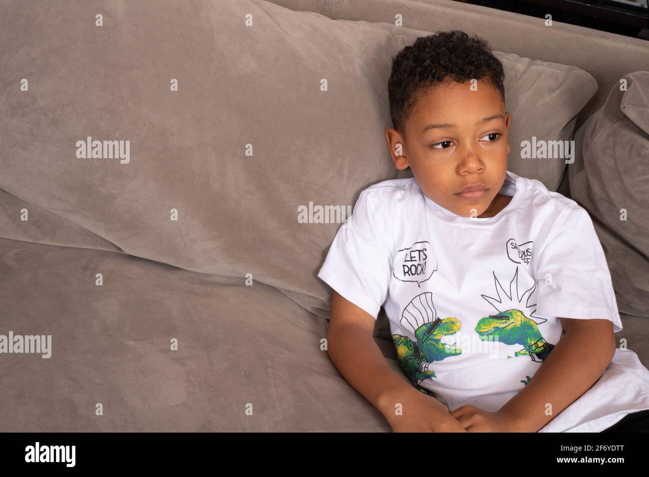 Ritratto di un ragazzo di 6 anni seduto da solo sul divano, guardando a fianco, triste, depresso, isolato Foto Stock