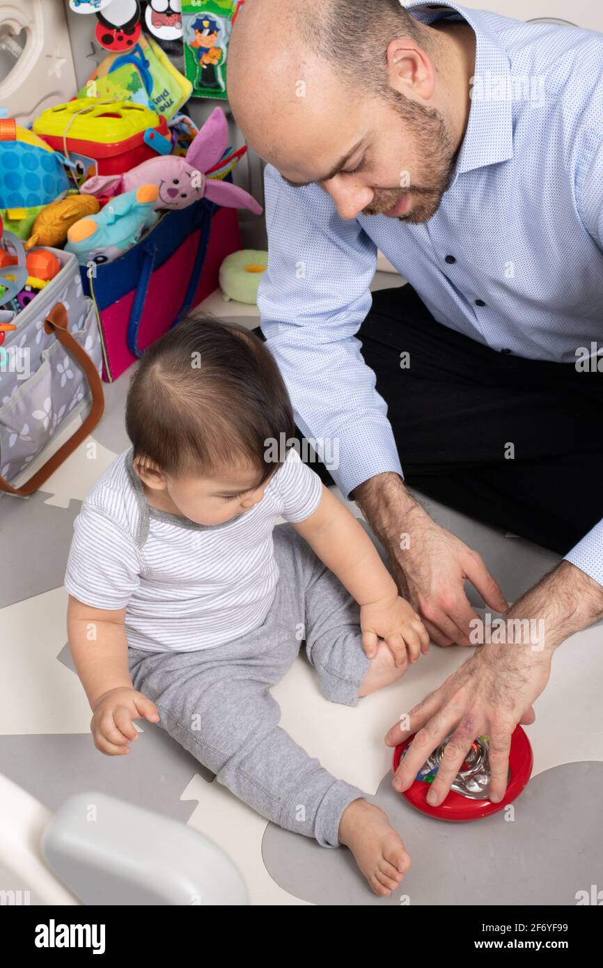bambino di 8 mesi, mostrato nuovo giocattolo da padre, filando o ruotando in modo che le perle all'interno si muovono Foto Stock