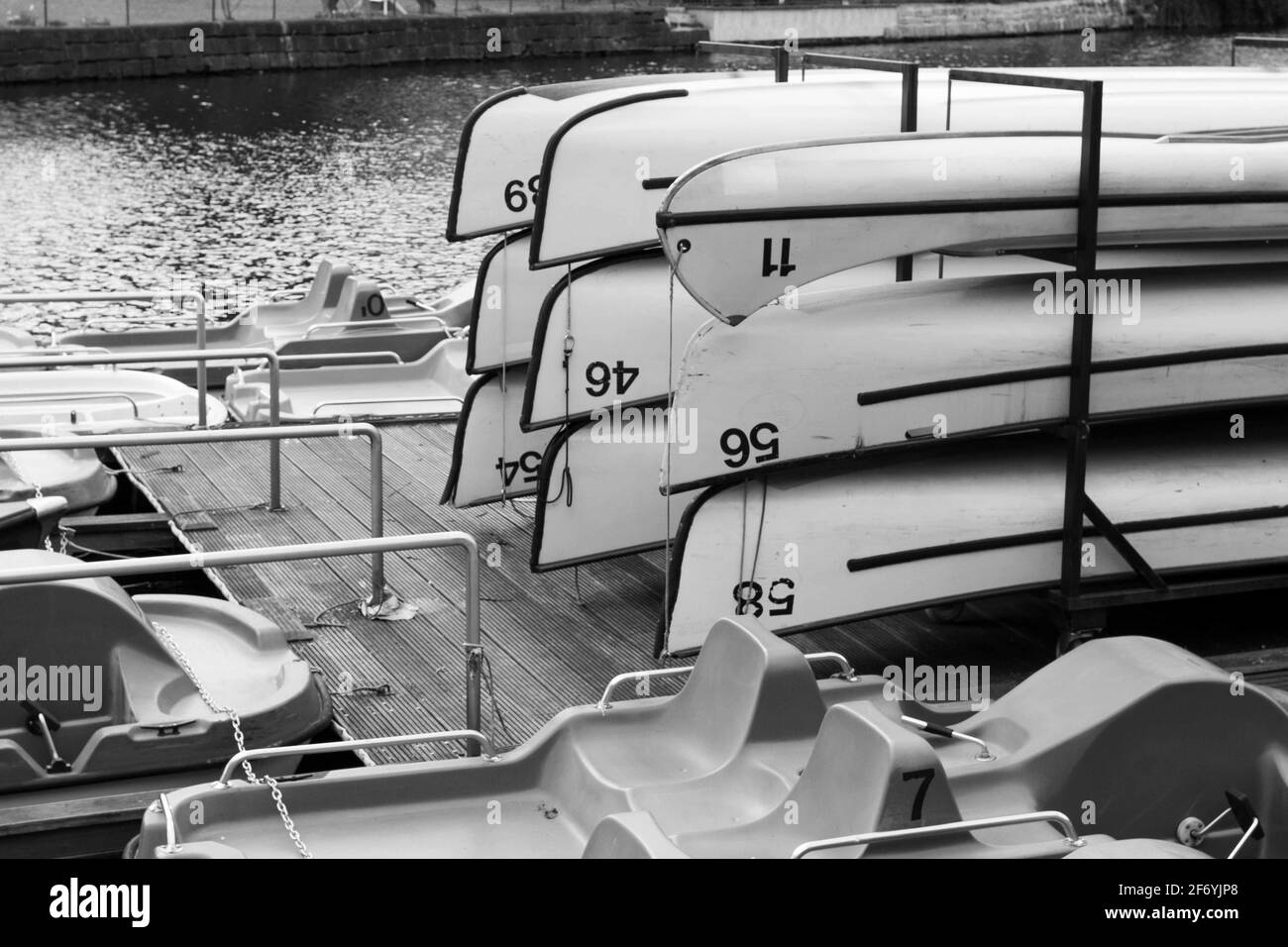 Fotografia in bianco e nero di nove canoe riposte capovolte su una rastrelliera su un molo a lato del fiume durante la decollo stagione Foto Stock