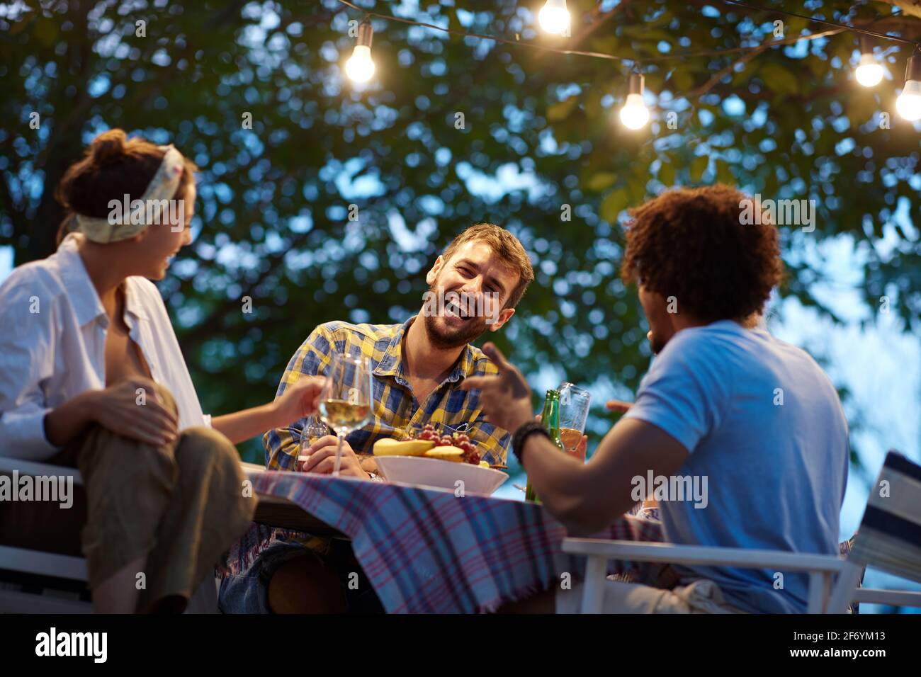 gruppo di amici multietnici che ridono, parlano, seduti al tavolo esterno Foto Stock