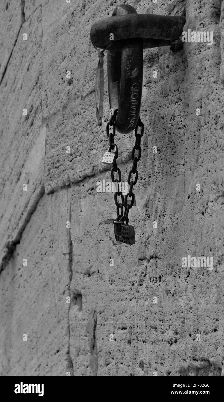 Particolare di una catena bloccata con lucchetti appesi ad un anello di ferro in un muro di pietra Foto Stock
