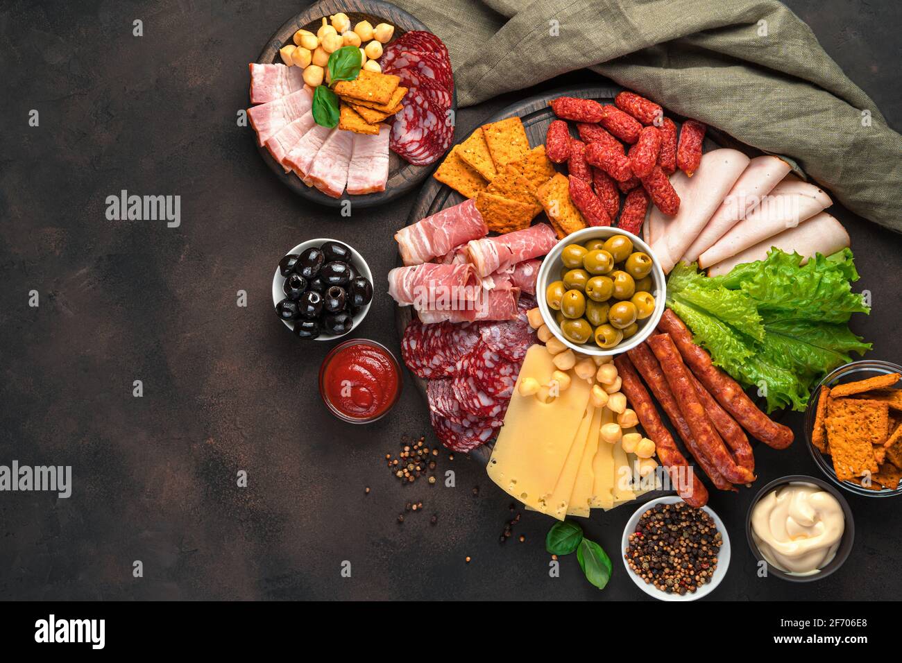 Prelibatezze di carne, salumi, salsicce di vario tipo, olive e salse su tavola marrone. Spuntini affumicati. Sfondo culinario, spazio di copia. Foto Stock