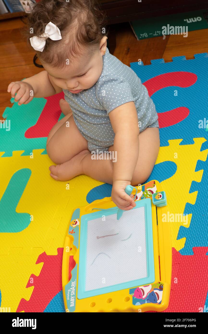 bambina di 7 mesi seduta e facendo segni con la bacchetta da disegno su una tavoletta simile a un attacco uno schizzo, utilizzando qualcosa come strumento Foto Stock