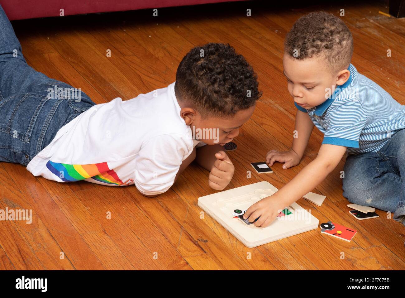 ragazzo di 3 anni che fa peg puzzle, osservato e aiutato da fratello di 7 anni Foto Stock