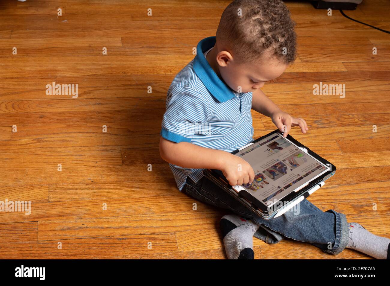 ragazzo di 3 anni seduto a terra utilizzando un dispositivo tablet Fornito dal programma Prek per uso domestico durante la pandemia di Covid-19 arresto Foto Stock