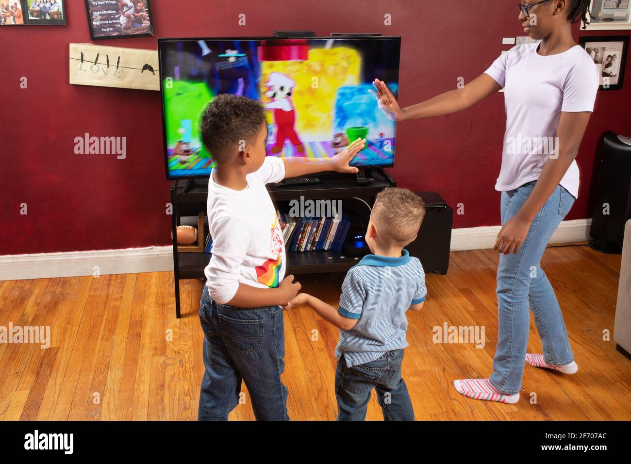 3 bambini di età 3, 7 e 12 anni, ballare e muoversi per fare esercizio o ballare video su schermo tv divertimento al coperto Foto Stock