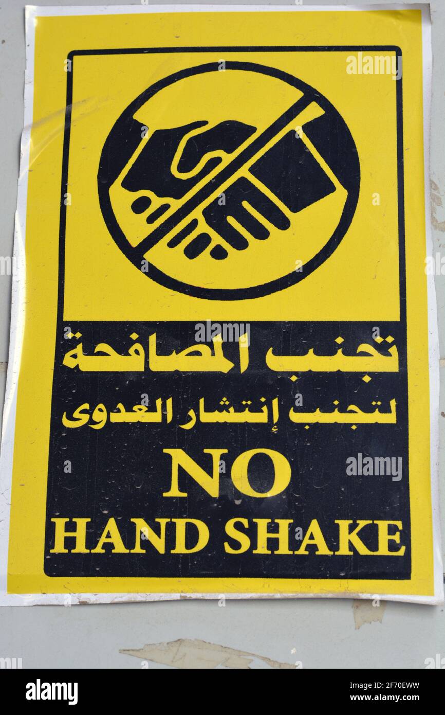 Adesivo da parete in arabo e inglese , traduzione di parole arabe (evitare di scuotere la mano per prevenire la diffusione di infezioni) , un segno da parete per prevenire il virus corona Foto Stock