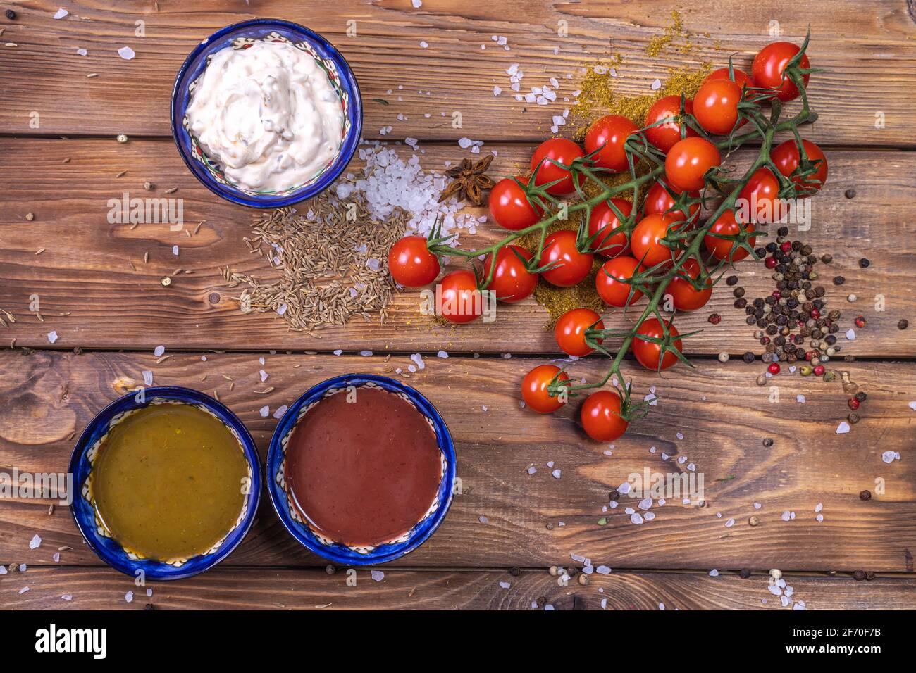 Salsa all'assortimento su fondo di legno marrone, decorata con pepe, pomodori ciliegini, spezie, sale grosso. Menu del ristorante. Foto Stock
