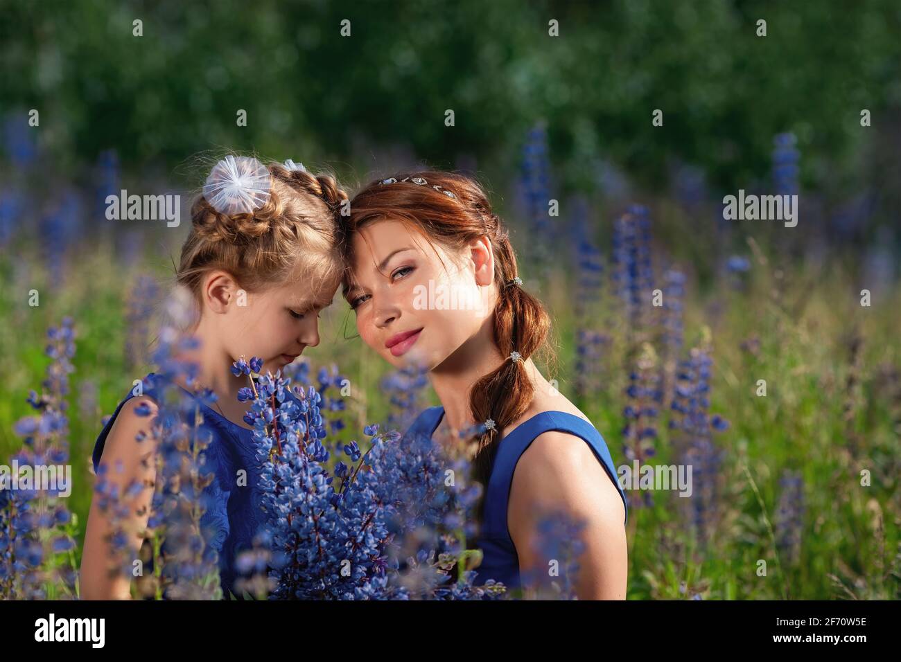 Felici le attività della famiglia e lo stile di vita all'aperto su un prato estivo soleggiato con erba e fiori blu. Bambina figlia seduta vicino a madre. M Foto Stock