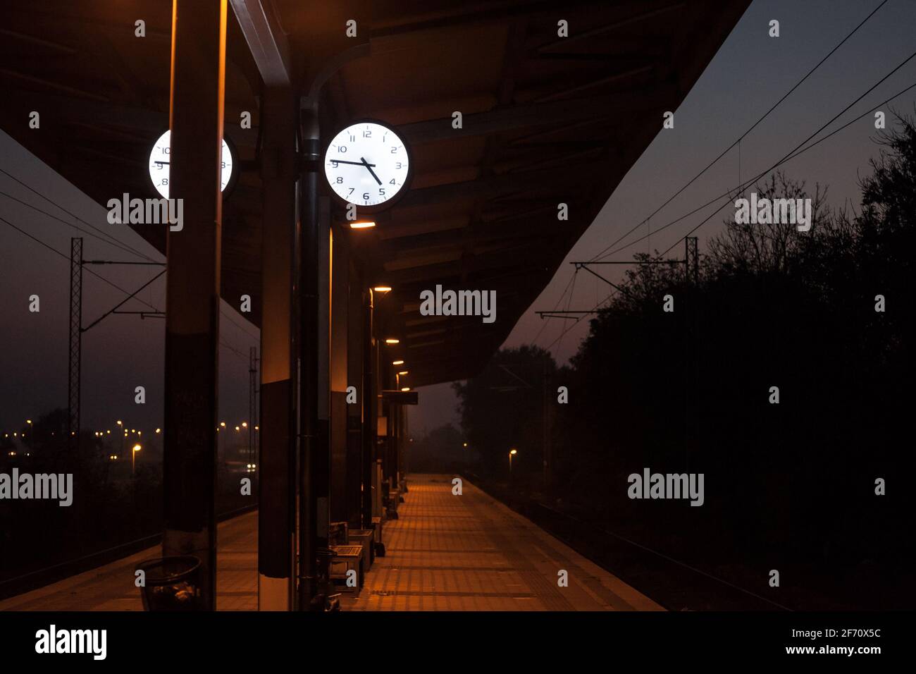 Orologio analogico sulla piattaforma di una stazione ferroviaria centrale di notte, durante una sera di tramonto buio, che indica l'orario preciso, di fronte a una t deserta Foto Stock