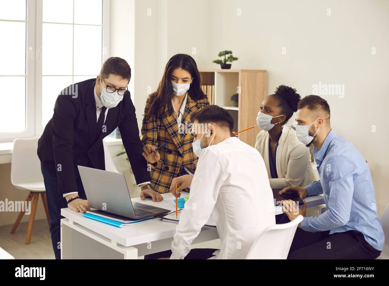 Team aziendale diversificato, tutti in maschere di fronte che lavorano sul loro progetto in riunione d'ufficio Foto Stock