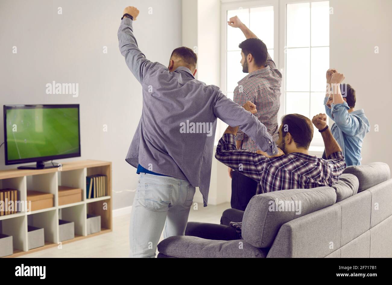Amici adulti maschi attivi con braccia alzate emotivamente guardando una partita di calcio in TV a casa. Foto Stock