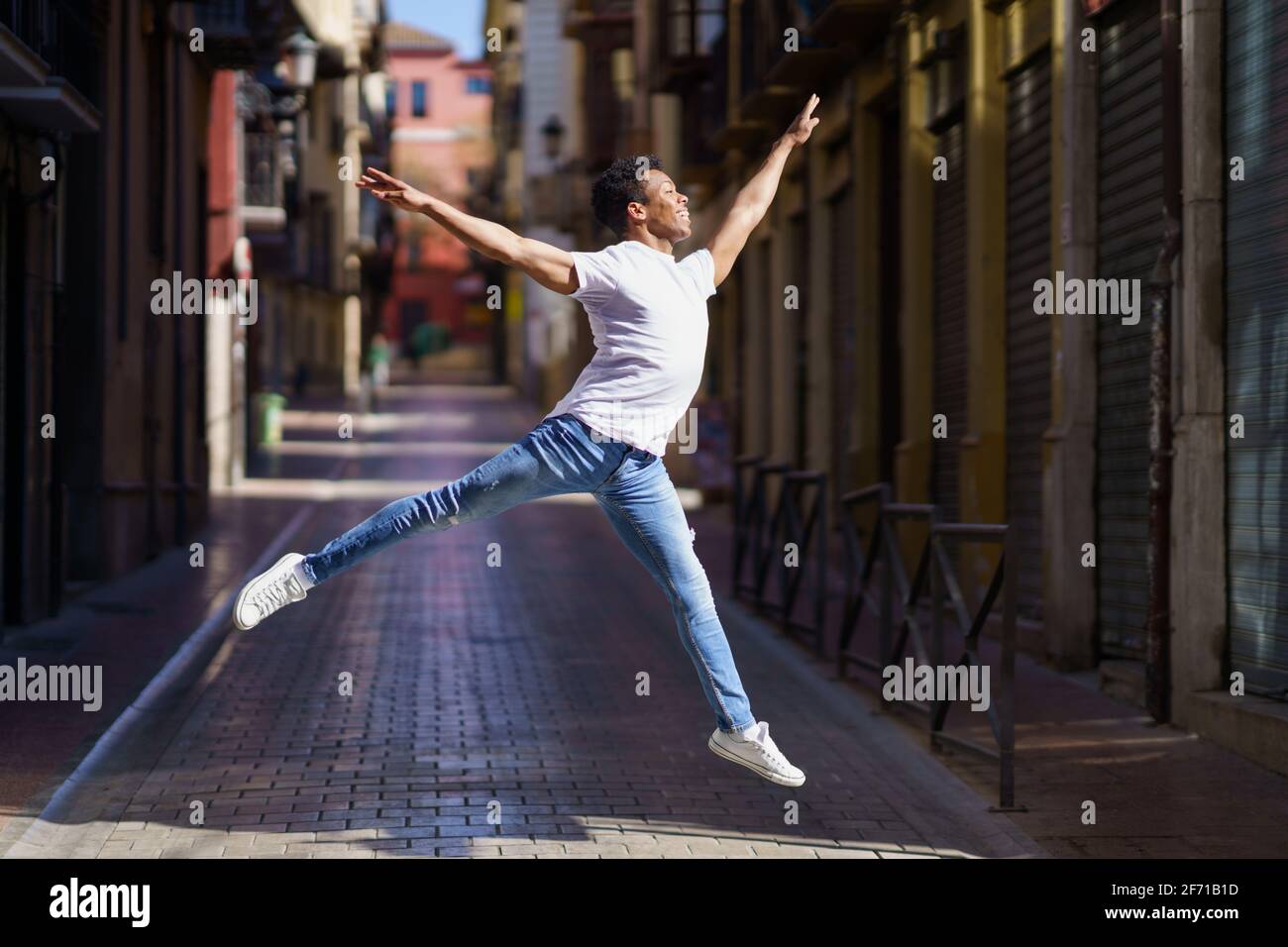 Un ragazzo nero felice che fa un salto acrobatico nel mezzo della strada. Foto Stock