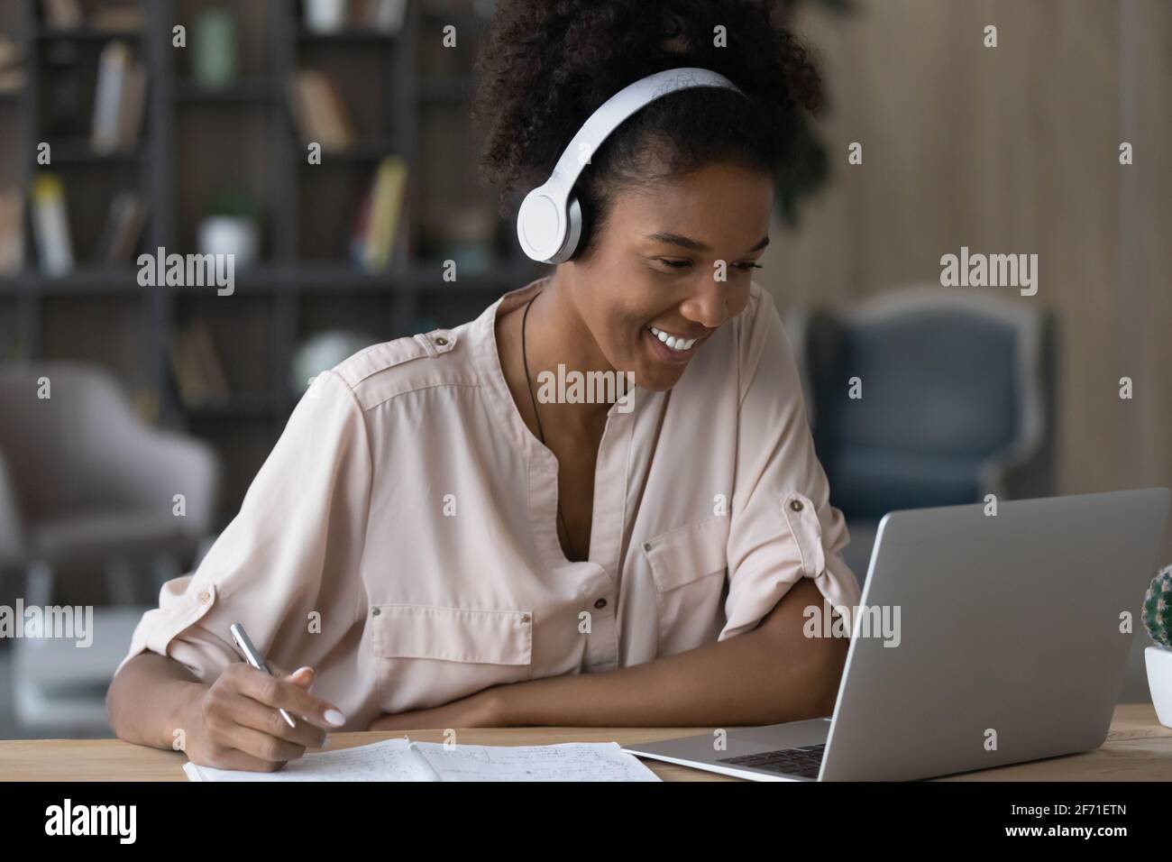 Sorridente studio femminile biraciale millenario su computer portatile Foto Stock