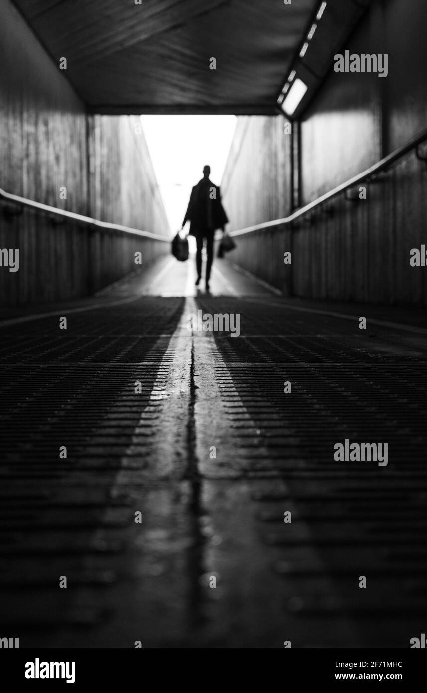 Uomo che cammina da solo con borse per la spesa in un tunnel Foto Stock