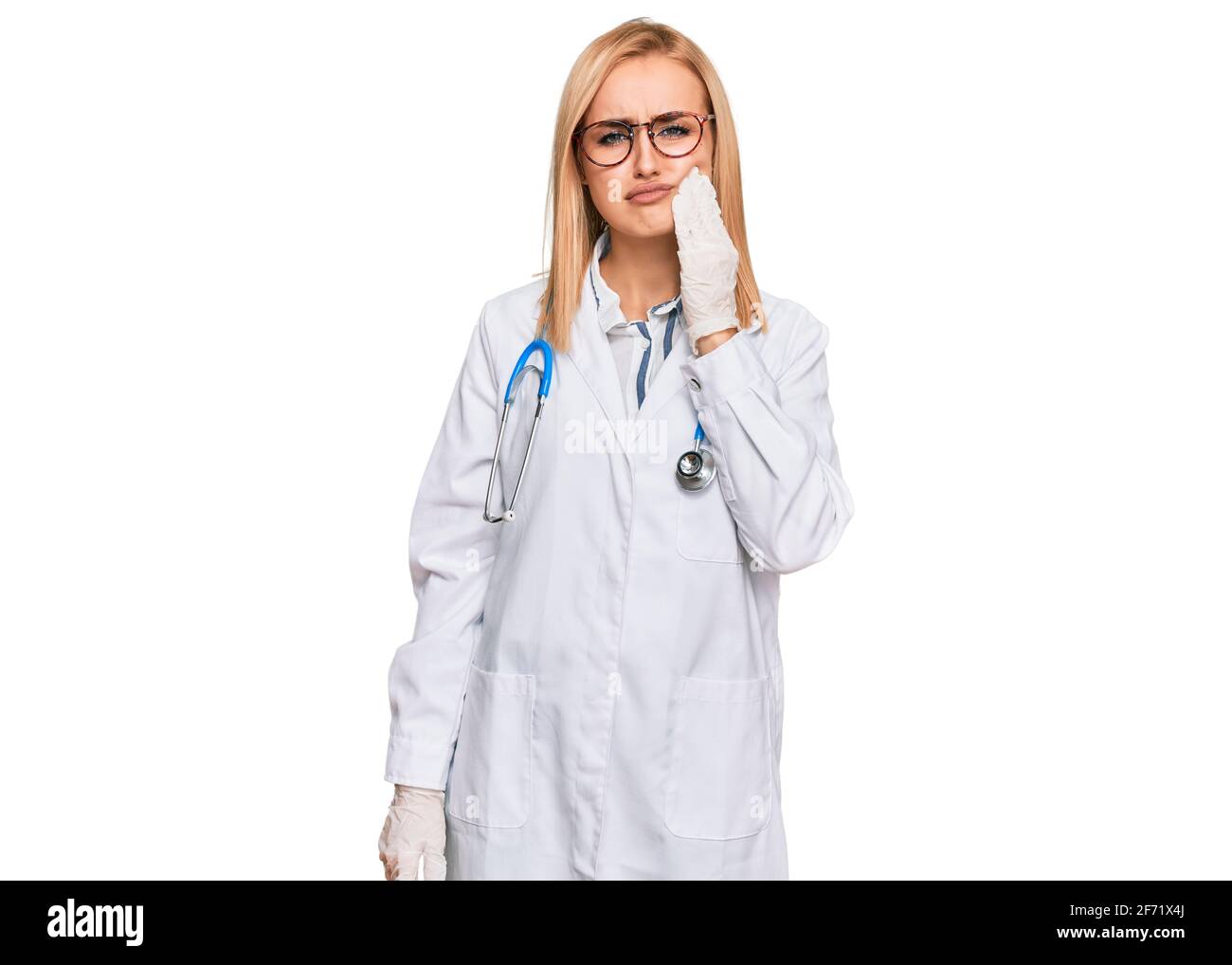Bella donna caucasica che indossa uniforme medico e stetoscopio che tocca la bocca con la mano con espressione dolorosa a causa di mal di denti o dentali illne Foto Stock