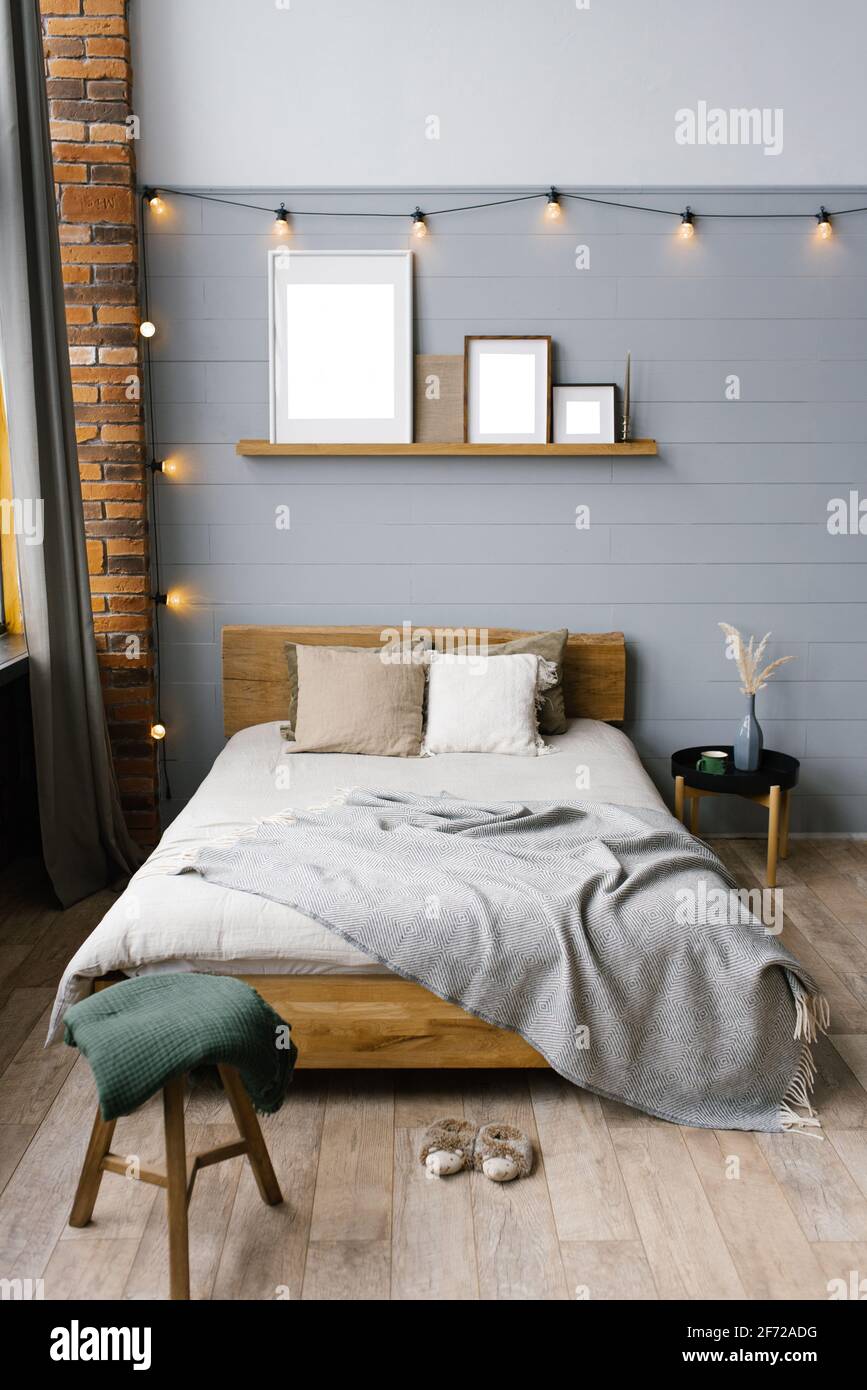 Letto matrimoniale con accenti naturali naturali sulle lenzuola e cuscini beige nella camera da letto grigia scandinava, spazio copia sui dipinti sullo scaffale abo Foto Stock