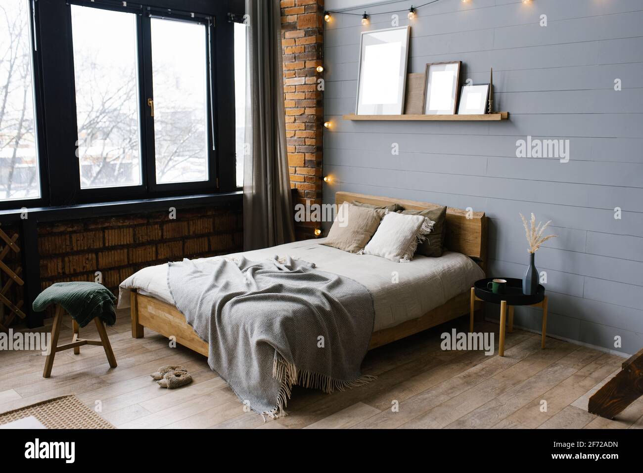 Letto matrimoniale con accenti naturali naturali sulle lenzuola e cuscini beige nella camera da letto grigia scandinava, spazio copia sui dipinti sullo scaffale abo Foto Stock