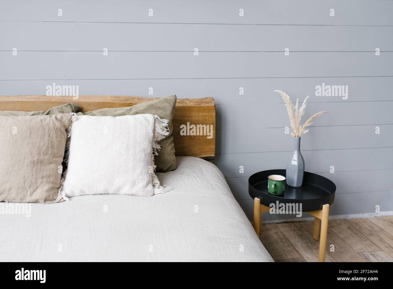 Moderno comodino nero accanto al letto matrimoniale con letti grigi in una semplice camera da letto interna Foto Stock