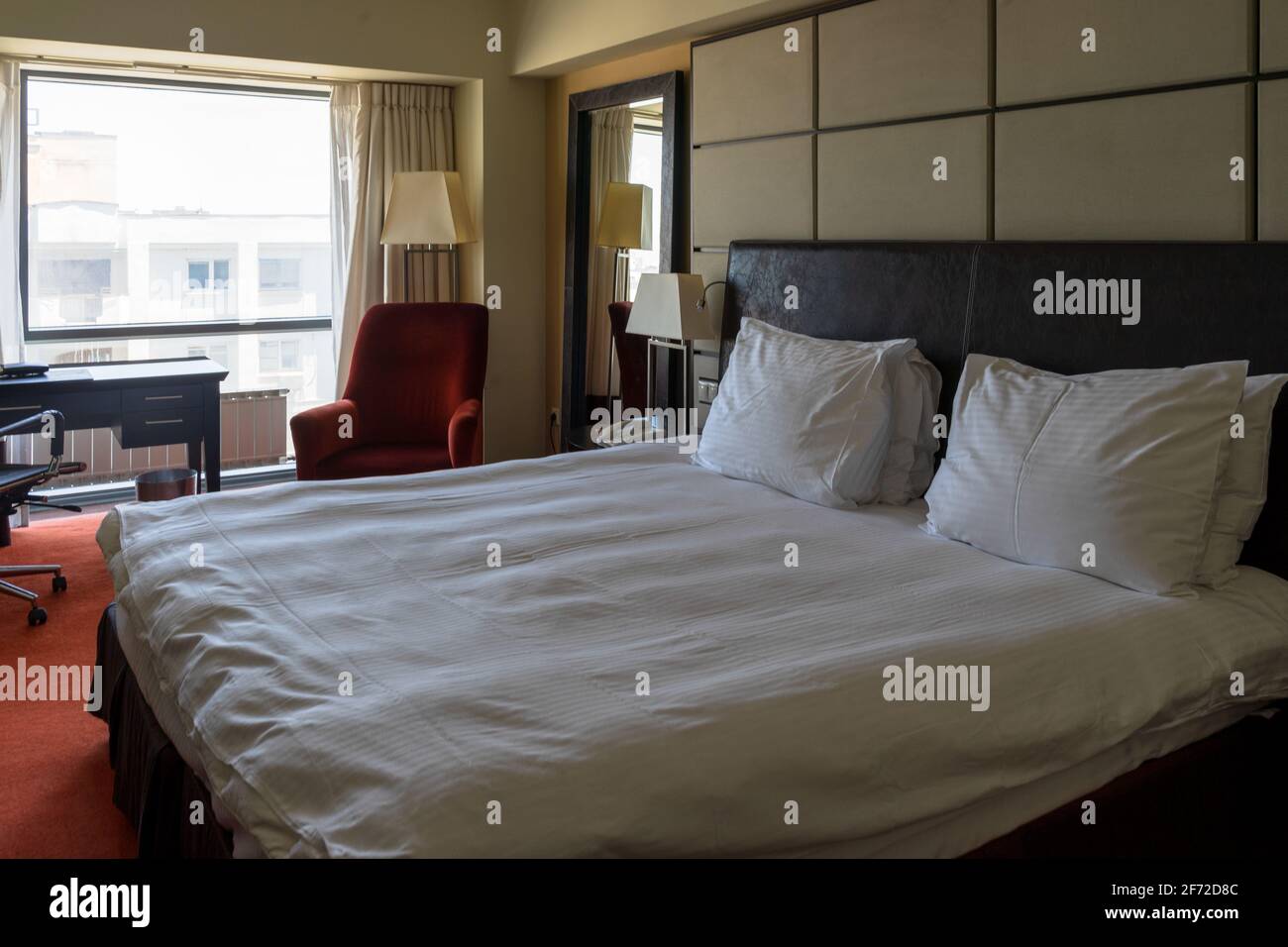 Moderna camera d'albergo o appartamento con letto king size appena fatto sotto la luce naturale del giorno dalla finestra. Foto Stock