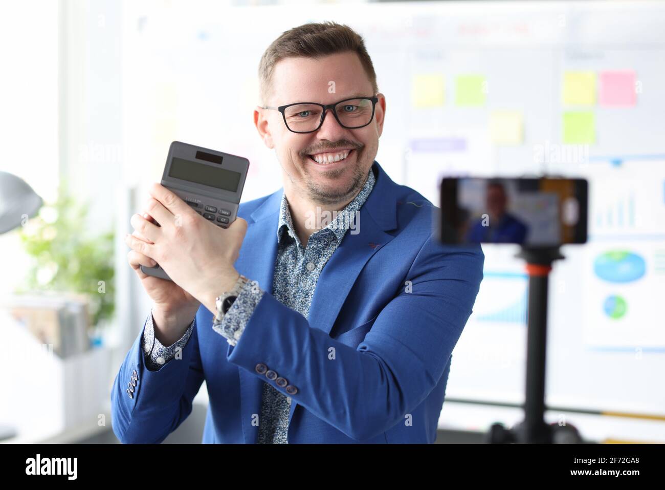 Un uomo d'affari sorridente tiene una calcolatrice e conduce corsi online su come aumentare i profitti Foto Stock