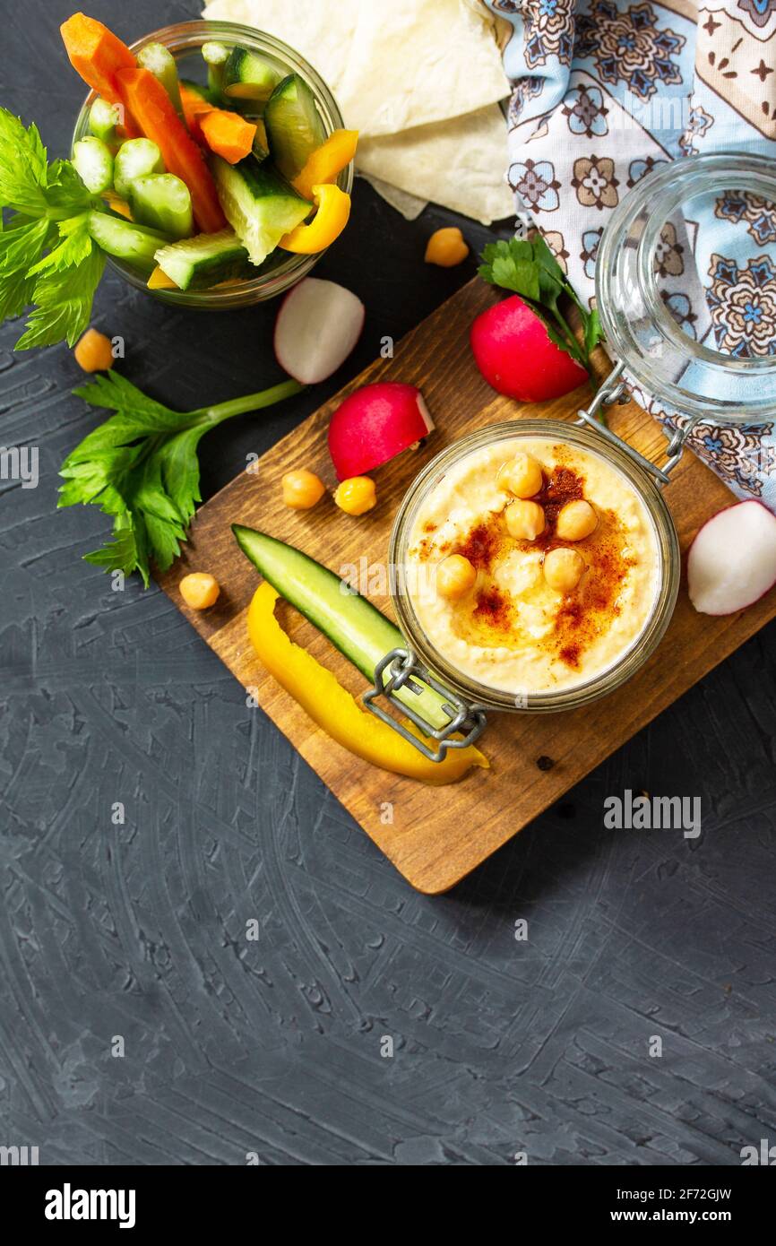Cucina araba. Hummus mediorientale con spuntini. Bagno di hummus con bastoncini di verdure fresche su un piano di pietra scuro. Vista dall'alto. Disposizione piatta. Spazio di copia. Foto Stock