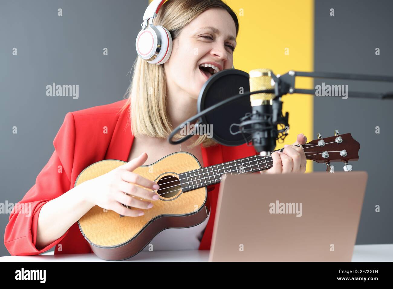 Donna canta e suona la chitarra con le cuffie davanti microfono Foto Stock