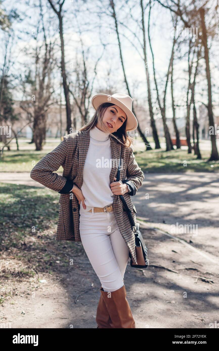 Bella donna che indossa blazer elegante, cappello e stivali che tengono  borsa nel parco. Primavera femminile outfit alla moda Foto stock - Alamy