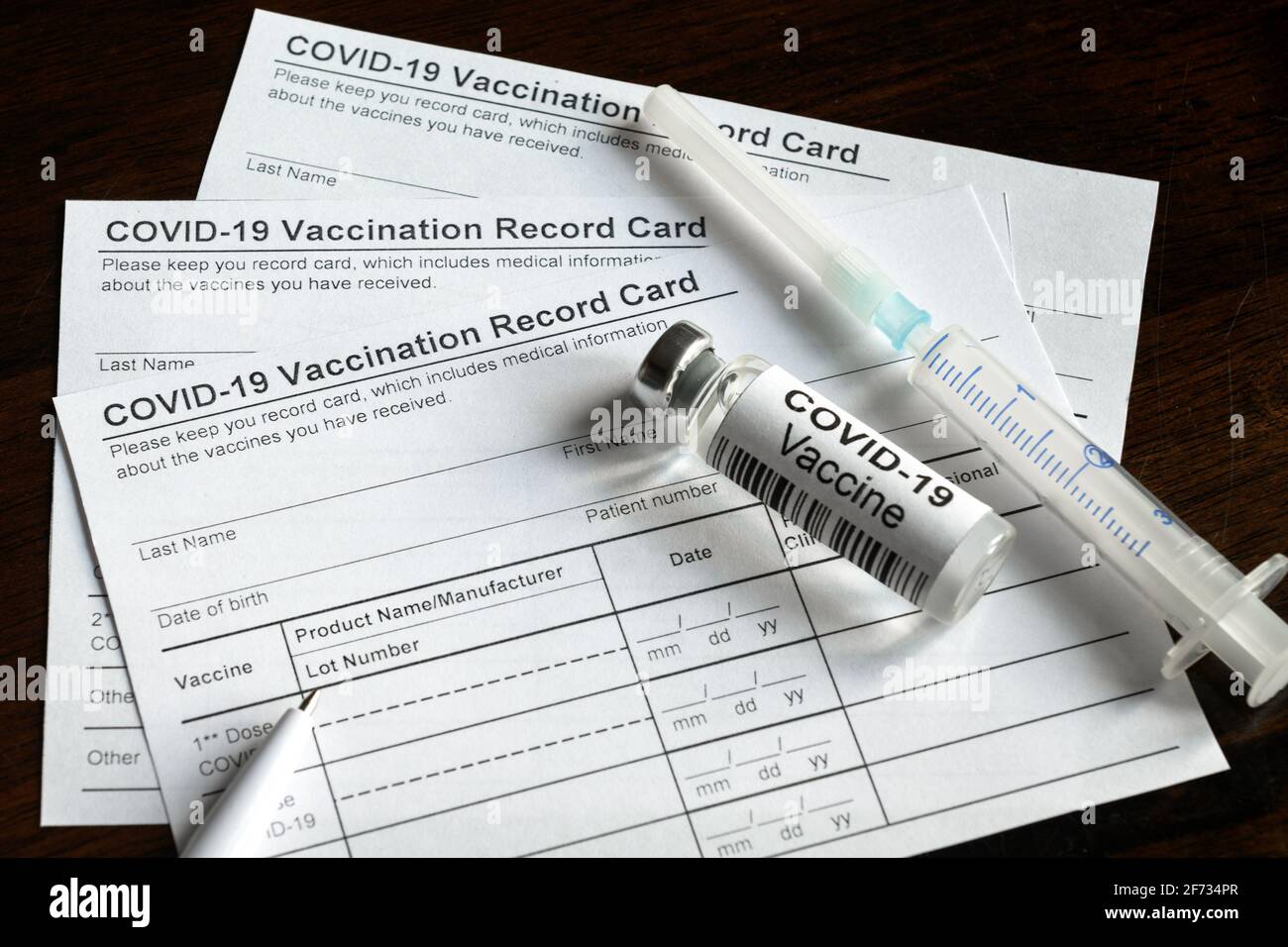 COVID-19 Vaccination Record Card su banco, certificato di immunizzazione con coronavirus e iniezione di vaccino. Siringa e flacone di vaccino per il virus corona sono Foto Stock