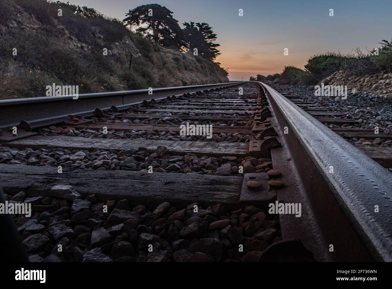I binari paralleli del treno conducono all'orizzonte mentre l'alba comincia a illuminare il cielo del mattino. Foto Stock