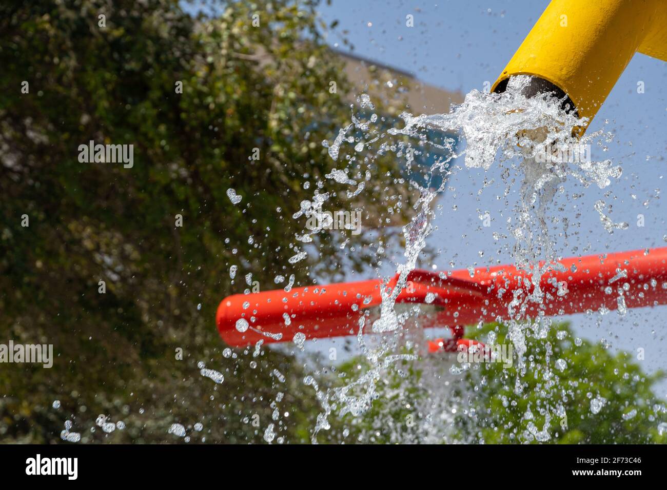 Divertimento estivo per i bambini al paraspruzzi per giocare con l'acqua che cade dalla fontana gialla di colore brillante alla piscina sottostante. Foto Stock