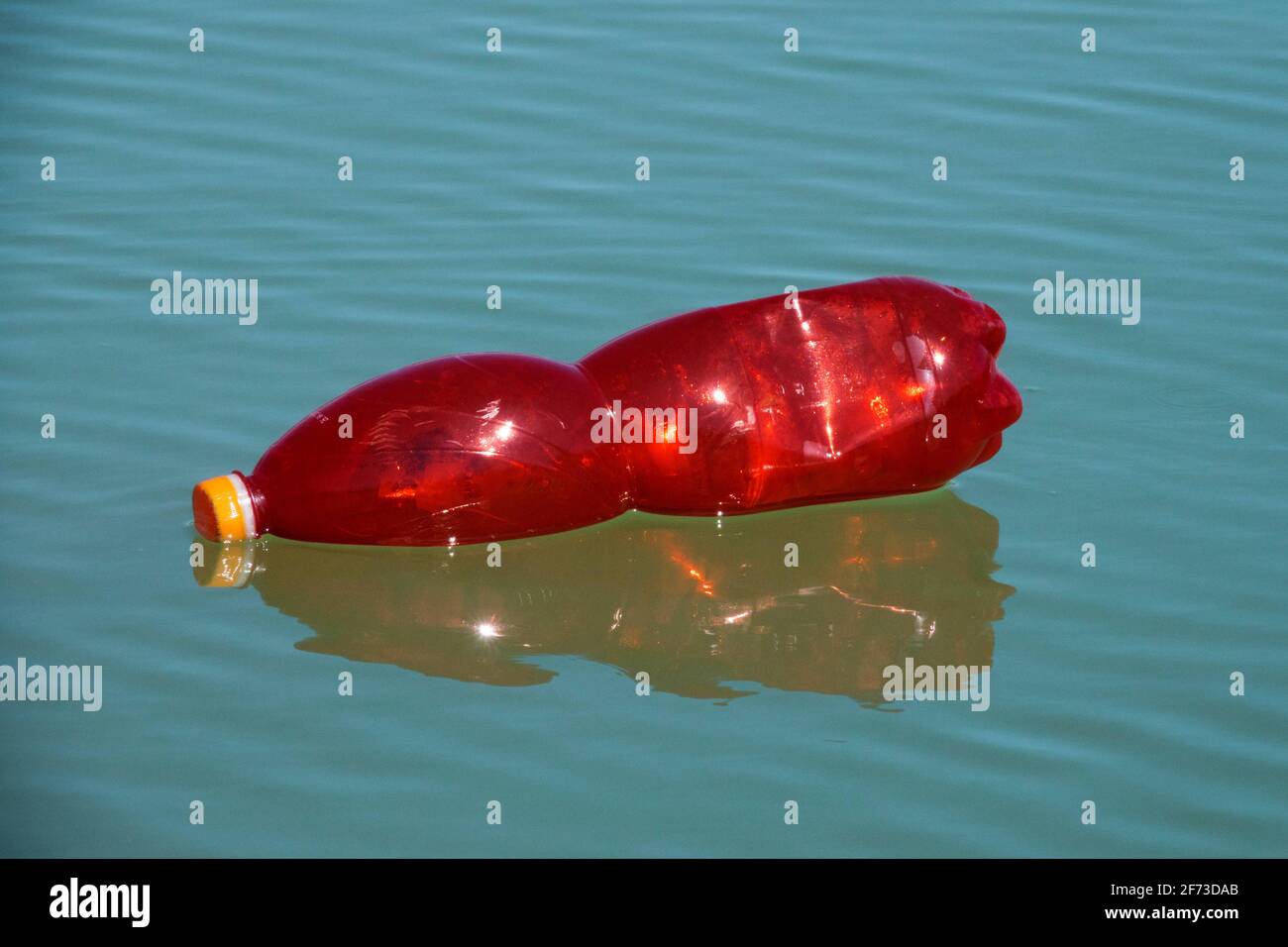 Bottiglia di plastica rossa che galleggia sull'acqua di superficie Foto Stock