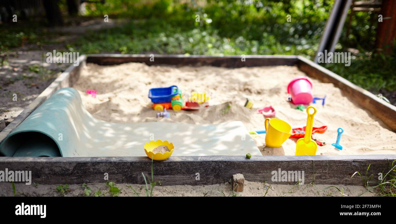 Sandbox all'aperto. Sandbox in legno per bambini con vari giocattoli per il gioco. Concetto estivo. Messa a fuoco selettiva con profondità di campo ridotta Foto Stock