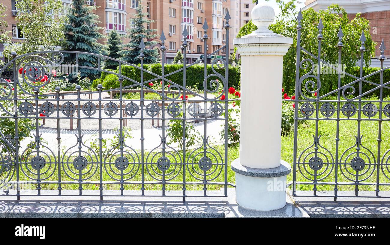 Recinzione in ferro battuto. Immagine di una bella recinzione decorativa in ghisa con forgiatura artistica e colonne in pietra Foto Stock