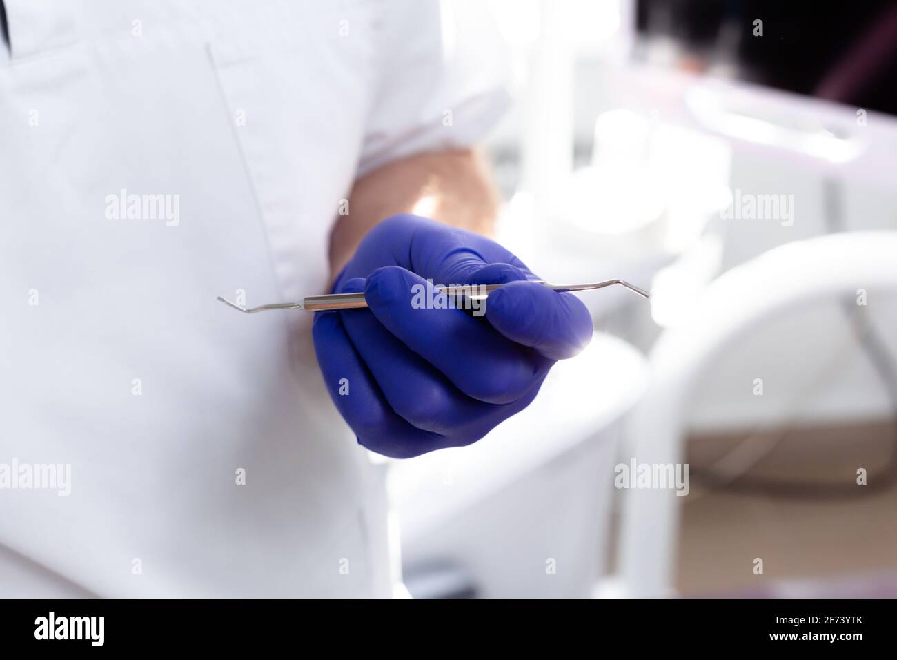 Le mani maschili in guanti medici blu tengono uno strumento dentale Foto Stock